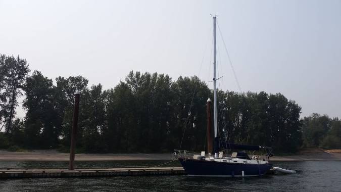 Single blue sailboat tied to a dock on a river with trees in the background