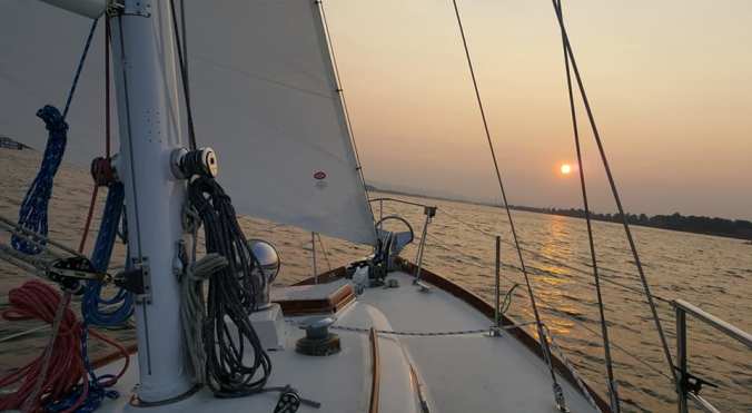 A view forward off the bow of the sailboat Mosaic sailing on the Columbia River with a gorgeous sunset on the horizon