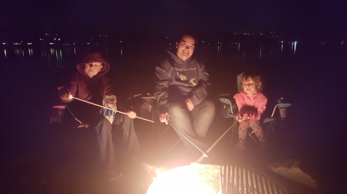 Mom, son, and daughter sitting around a campfire at night