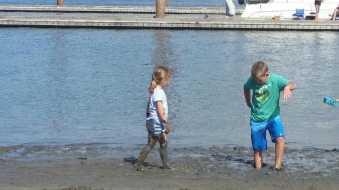 a boy and a girl playing in the mud along the riverbank