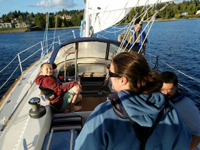 A woman at the helm of a sailboat under sail, with kids enjoying the ride