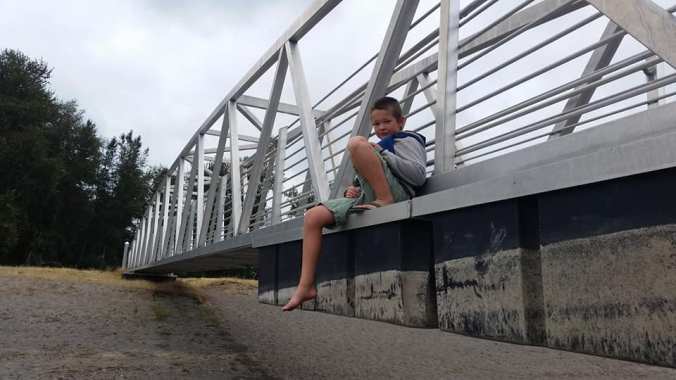 Boy hanging out, sitting on the outside of a dock ramp wearing a lifejacket and shorts
