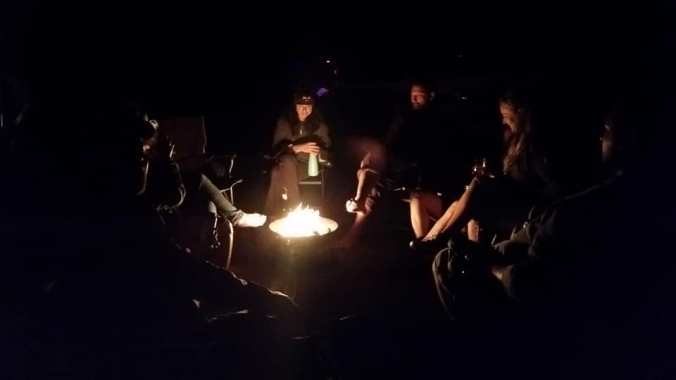 Large group of adults sitting around a campfire in the dark