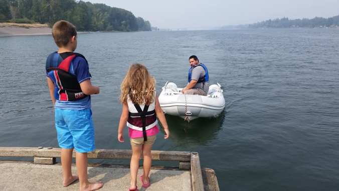 A boy and a girl standing on a dock watching their father approach in the inflatable dinghy