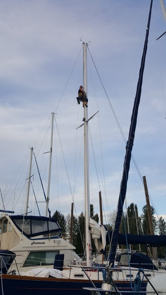 Woman 40-feet up the mast of a blue sailboat