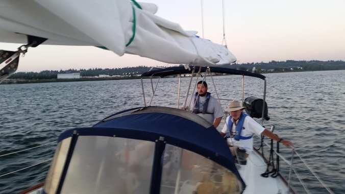 Looking back over the dodger of a sailboat at two men in the cockpit